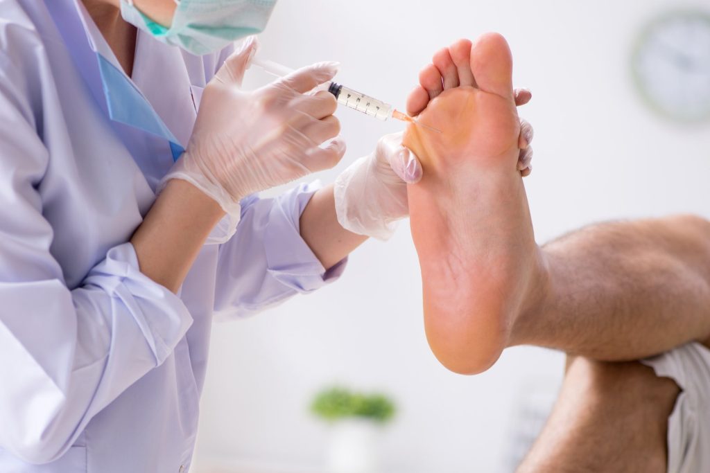 Doctor giving an injection into the bottom of a right foot