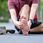 Person holding their heel in pain, illustrating plantar fasciitis and Achilles conditions